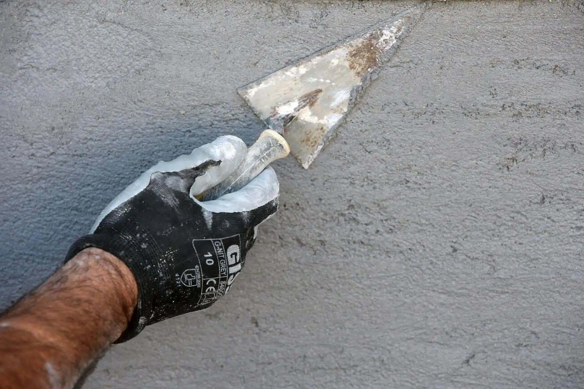 Gros plan sur la main d'un maçon appliquant du plâtre sur un mur , détail sur la truelle et les gants de protection.